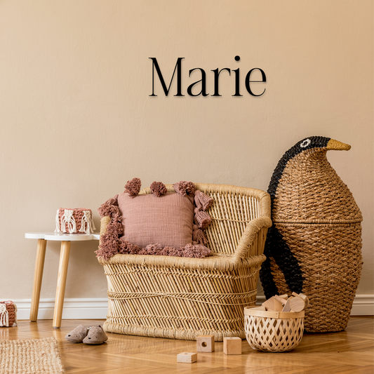 Wicker chair with pink cushion and decorative items against a beige wall with 'Marie' text. Acrylic wall decor - Vibewall