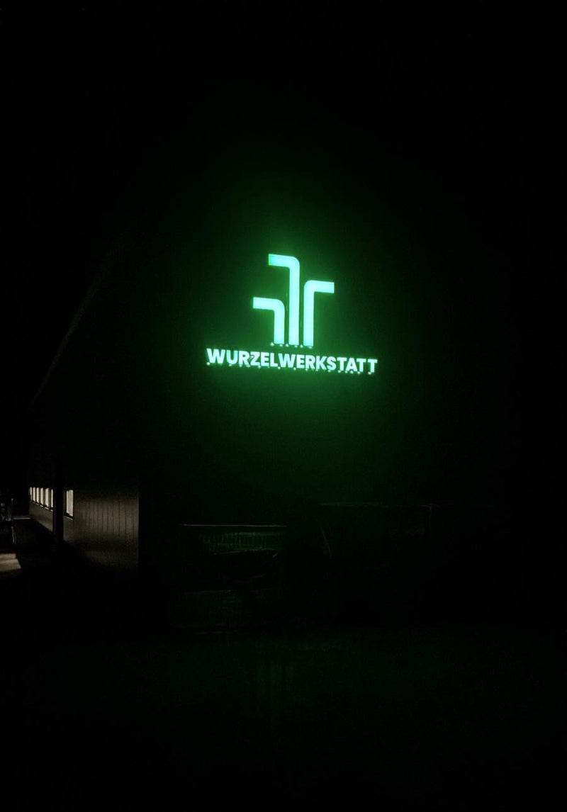 Green logo and text 'Wurzelwerkstatt' on a building in the dark.