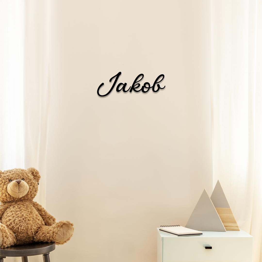Teddy bear on a chair next to a wall with the name 'Jakob' above, against a light beige curtain backdrop. Acrylic wall dekor - Vibewall