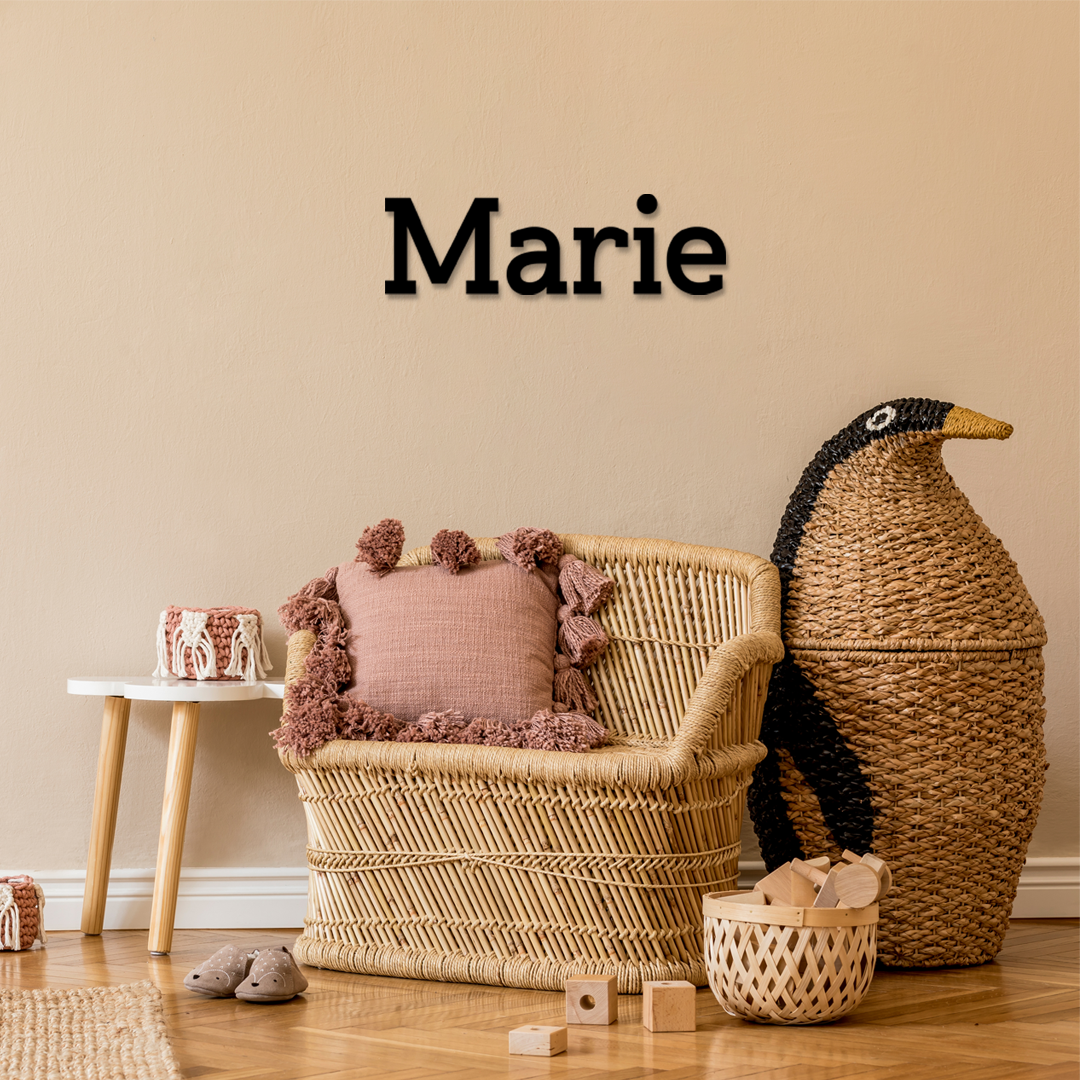 Wicker chair with pink cushion, wicker basket, and decorative items against a beige wall with 'Marie' decal. Acrylic wall decor - Vibewall