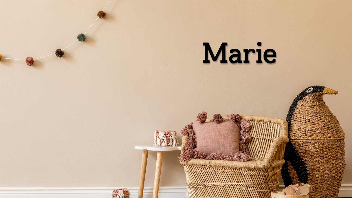 Decorative room with wicker chair, pink pillow, and decorative penguin against a beige wall with 'Marie' text. Acrylic wall decor - Vibewall