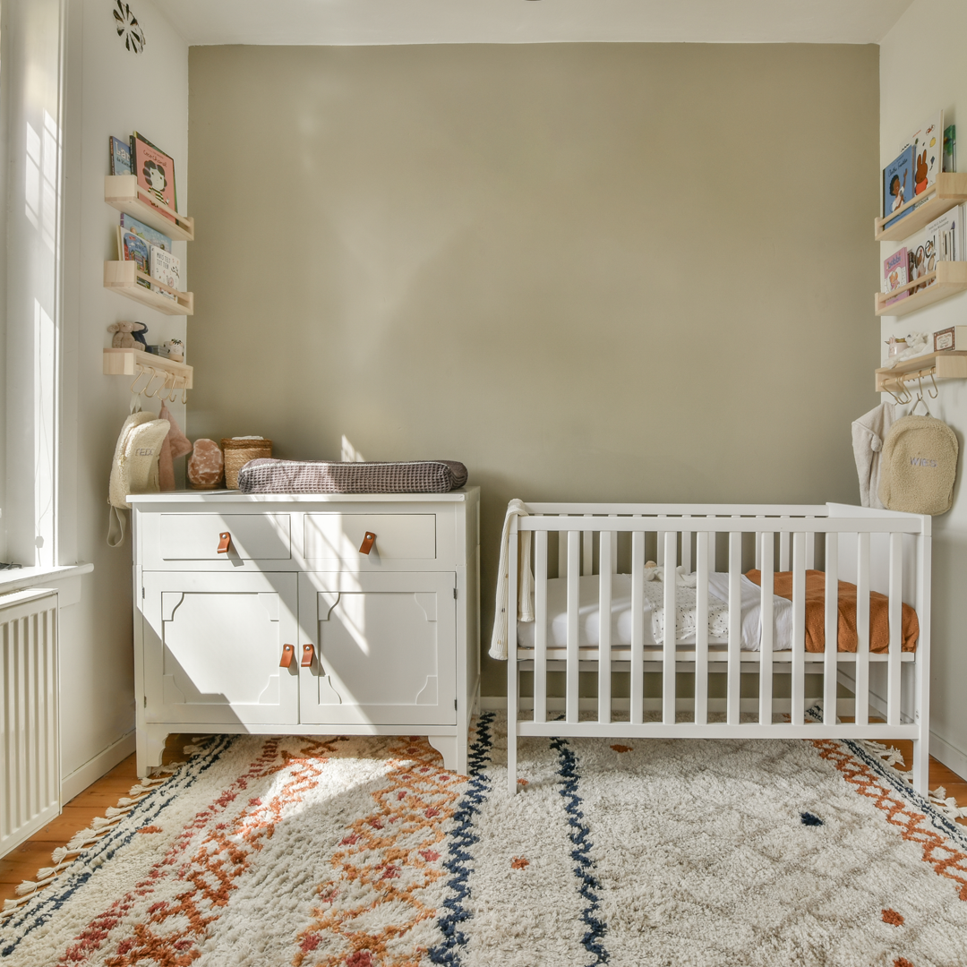 Nursery room with white crib and dresser against a beige wall.