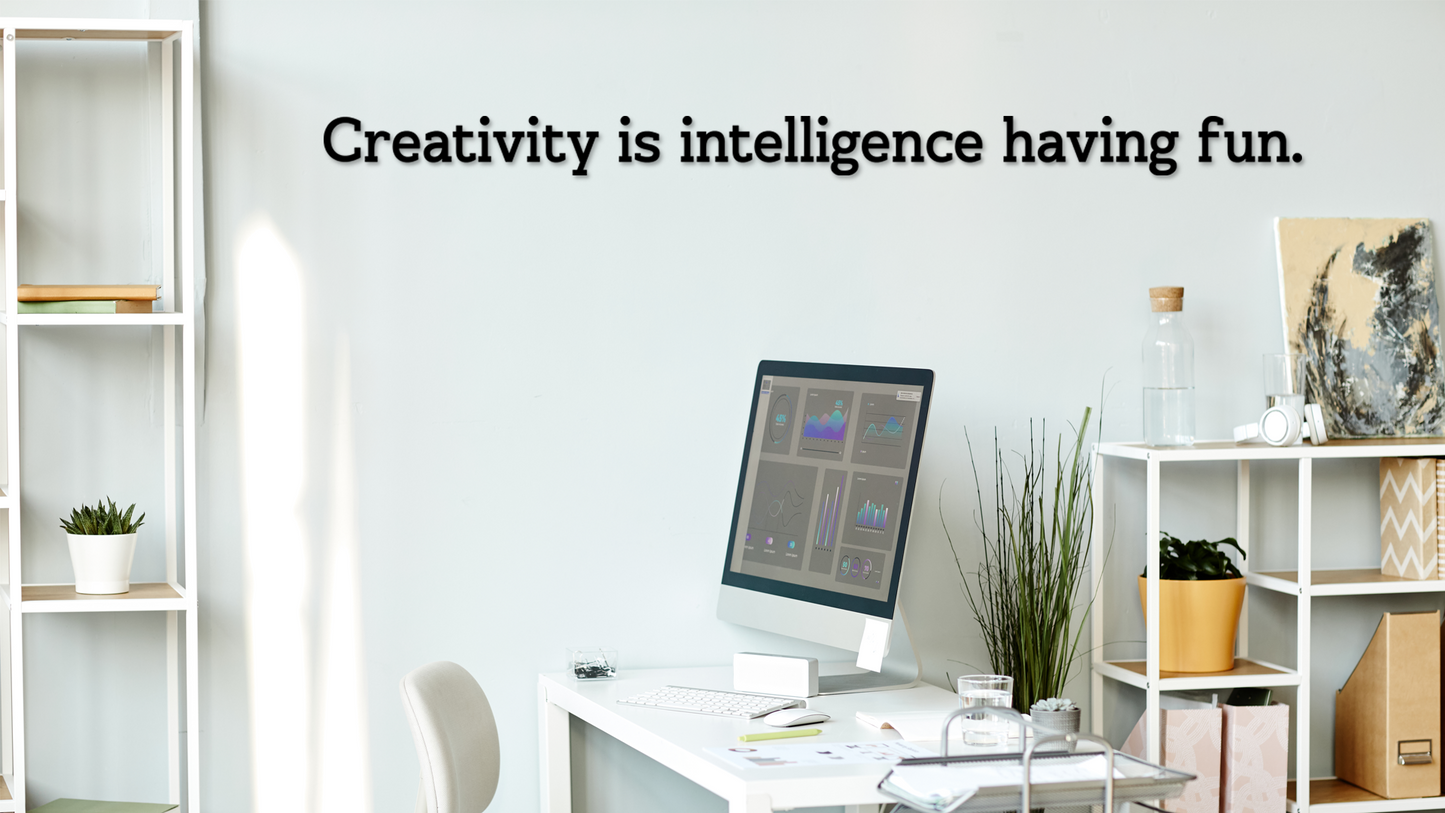 Modern office space with a desk, computer, and decor elements, featuring the quote 'Creativity is intelligence having fun.' Acrylic wall decor - Vibewall
