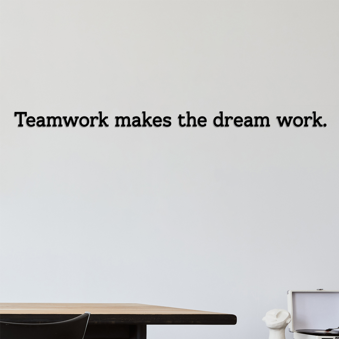 Motivational quote 'Teamwork makes the dream work' on a plain wall with a desk and chair in the foreground. Acrylic wall decor - Vibewall