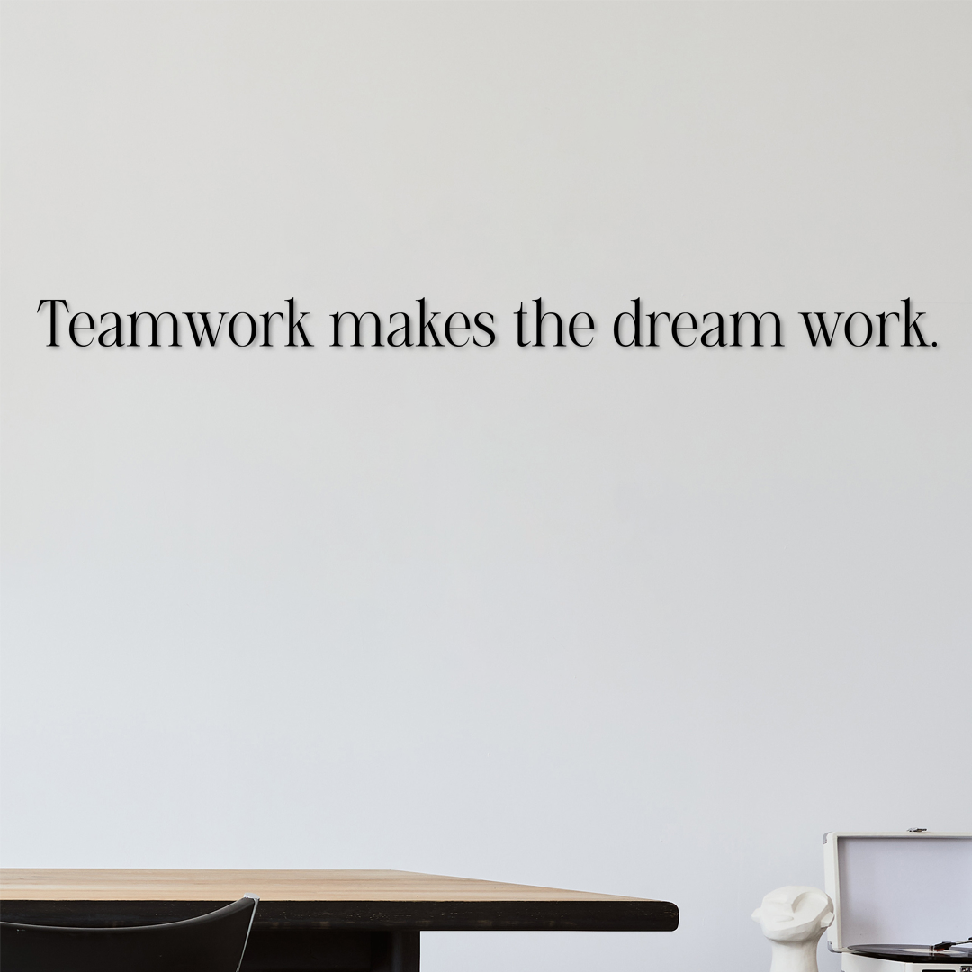 Motivational quote 'Teamwork makes the dream work' on a light gray wall with a desk and chair in the foreground. Acrylic wall decor - Vibewall