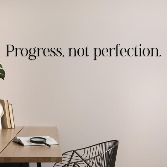 Minimalist office setup with 'Progress, not perfection.' quote on a beige wall. Acrylic wall decor - Vibewall