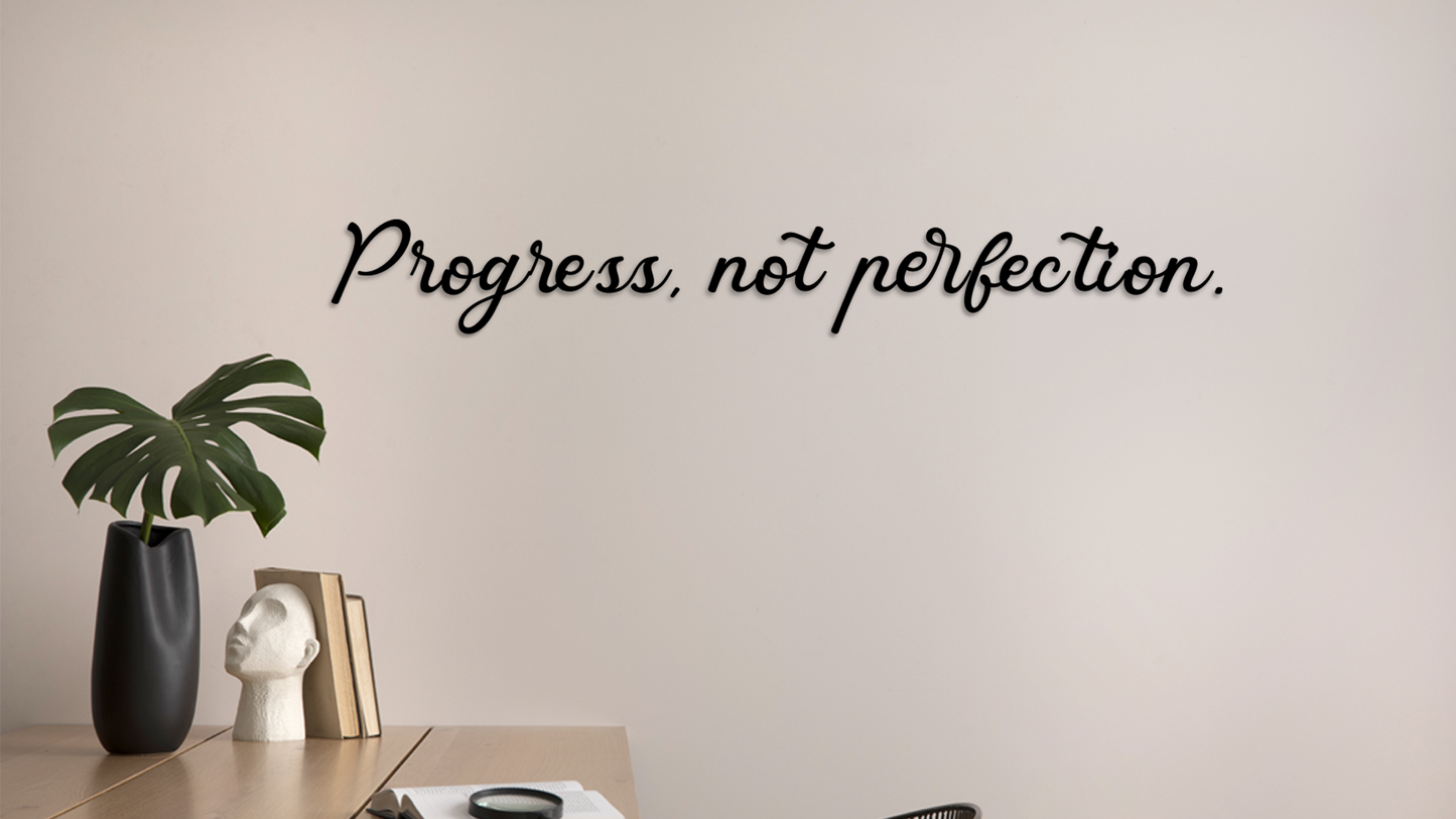 Wall with motivational quote 'Progress, not perfection.' and decorative items on a table. Acrylic wall decor - Vibewall