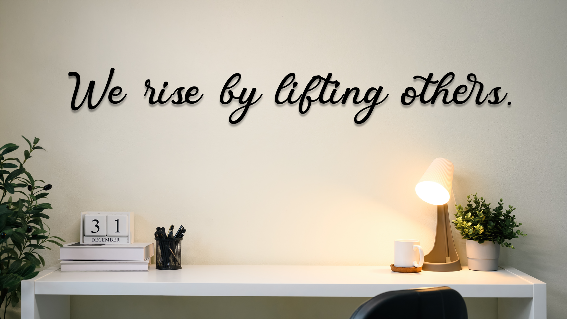 Decorative wall art with motivational quote 'We rise by lifting others' in a home office setting. Acrylic wall decor - Vibewall