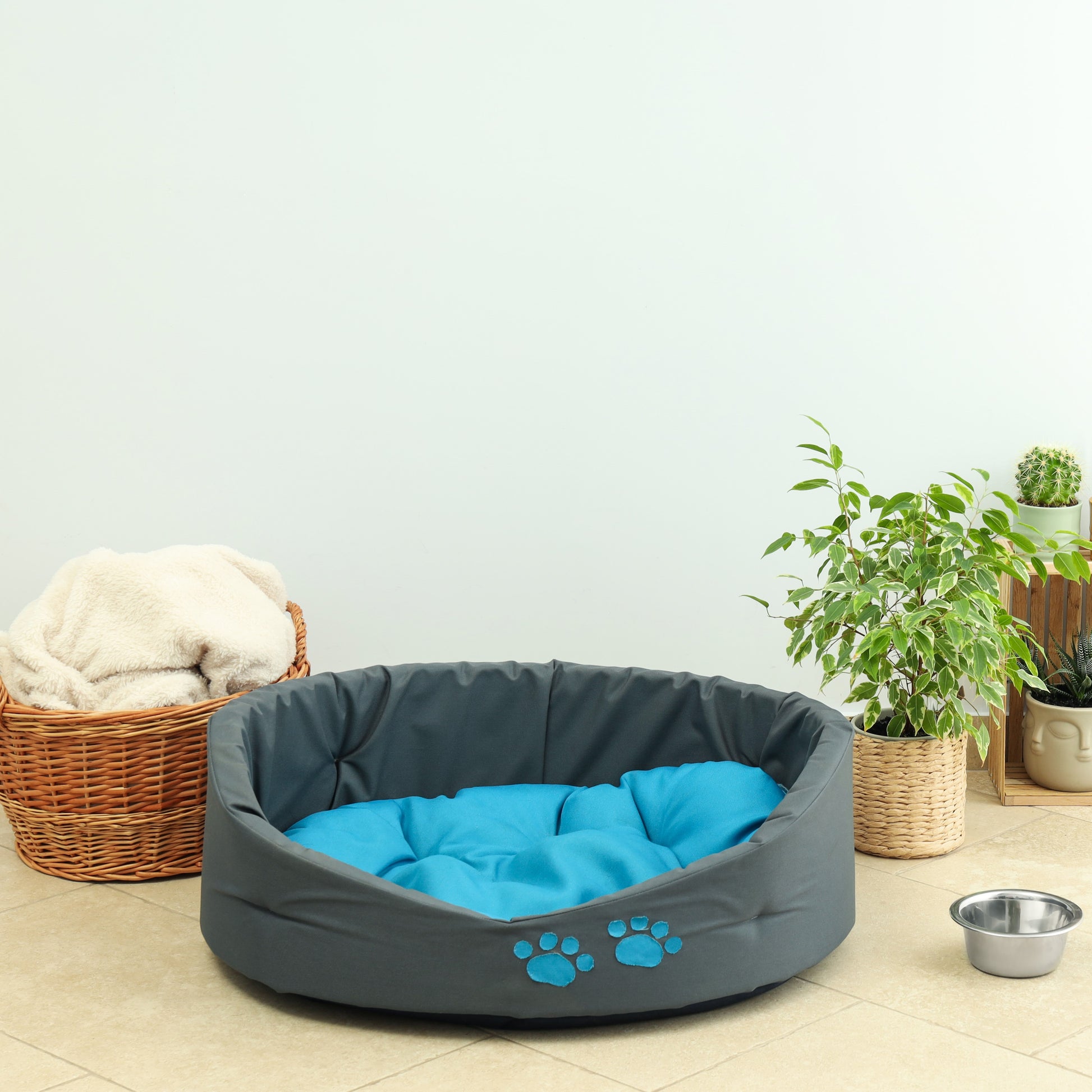 Gray pet bed with blue padding on a light wooden floor, surrounded by a basket, plants, and a small bowl. Background for Vibewall